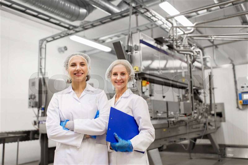 Manufacture, industry and people concept - happy women technologists with clipboard at ice cream factory shop, stock photo