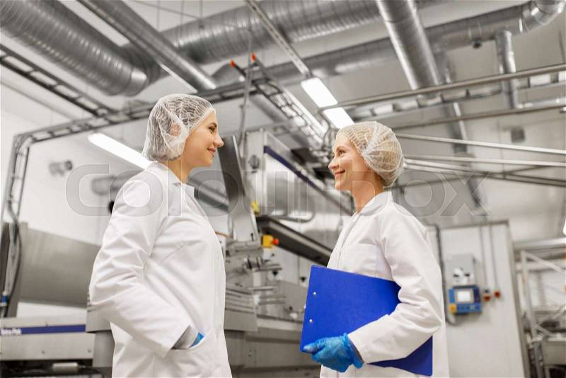 Manufacture, industry and people concept - happy women technologists with clipboard at ice cream factory shop, stock photo