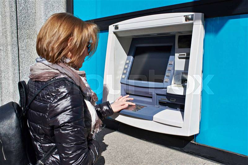 Woman enters a PIN code in an ATM, stock photo