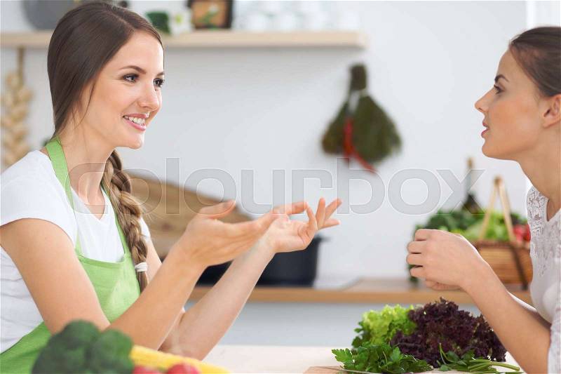 Two women friends cooking in kitchen while having a pleasure talk. Friendship and Chef Cook concept, stock photo