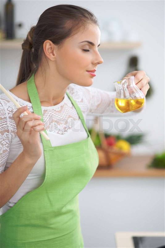 Young woman smelling the vegetable oil while enjoys cooking in the kitchen, stock photo