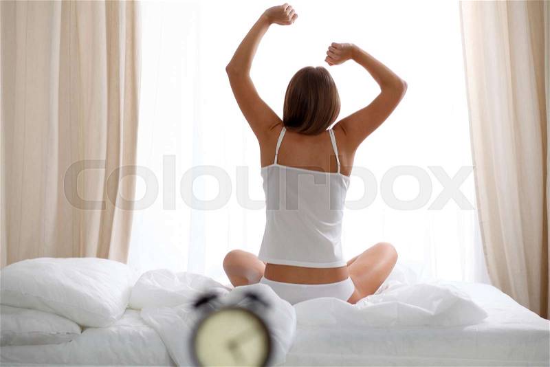 Woman stretching in bed after wake up, back view, entering a day happy and relaxed after good night sleep. Sweet dreams, good morning, new day, weekend, holidays concept, stock photo