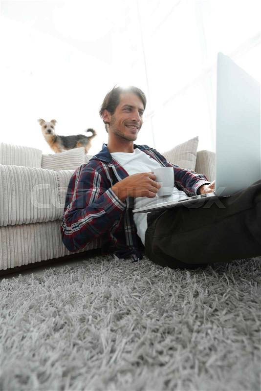 Young man is drinking tea sitting on the floor near the sofa. concept of a lifestyle, stock photo