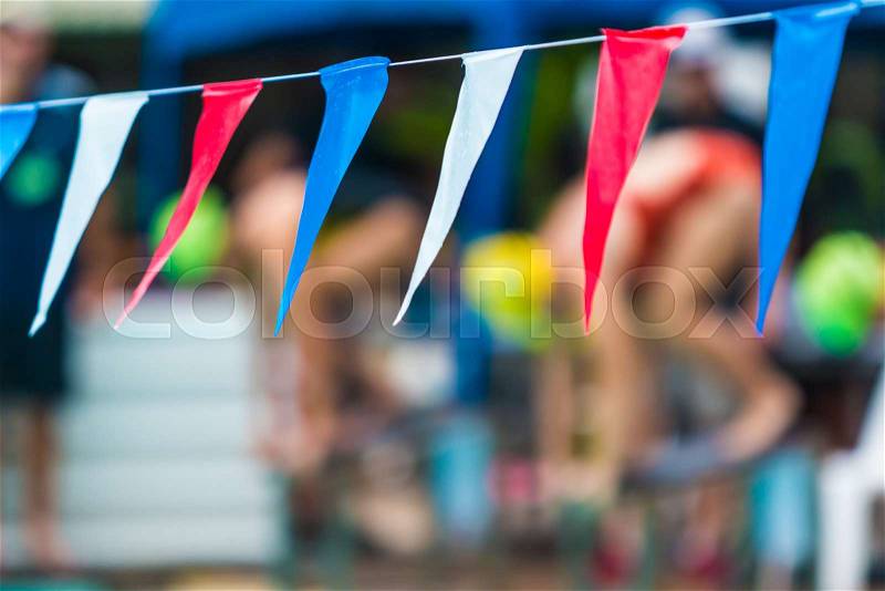 Sport multi-color sling flags hanging over swimming pool, selective focus on the middle blur flag with blurred background of swimmers getting ready to start, sport or competition concept, stock photo