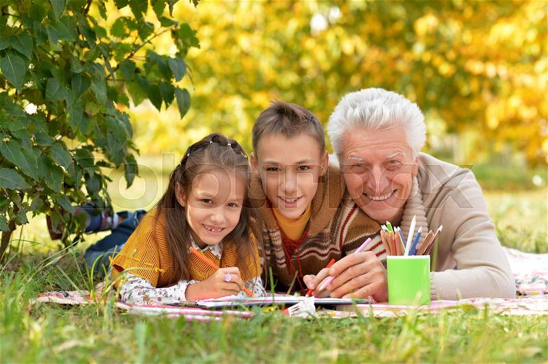 Portrait of children and grandfather doing homework in park, stock photo