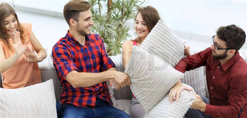 Friends playing pillow fight, sitting on the couch in the living room, stock photo