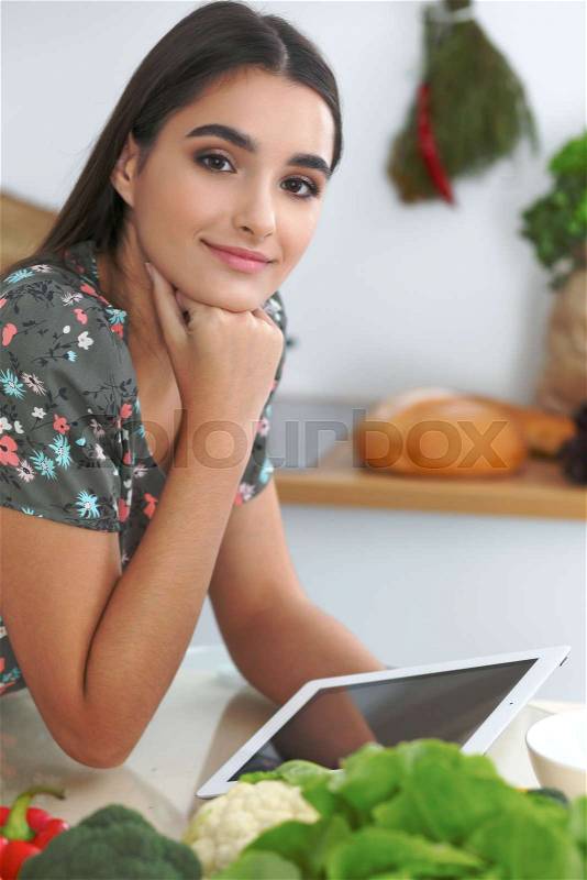Young hispanic woman or student cooking in kitchen. Girl using tablet to make online shopping or find a new recipe, stock photo