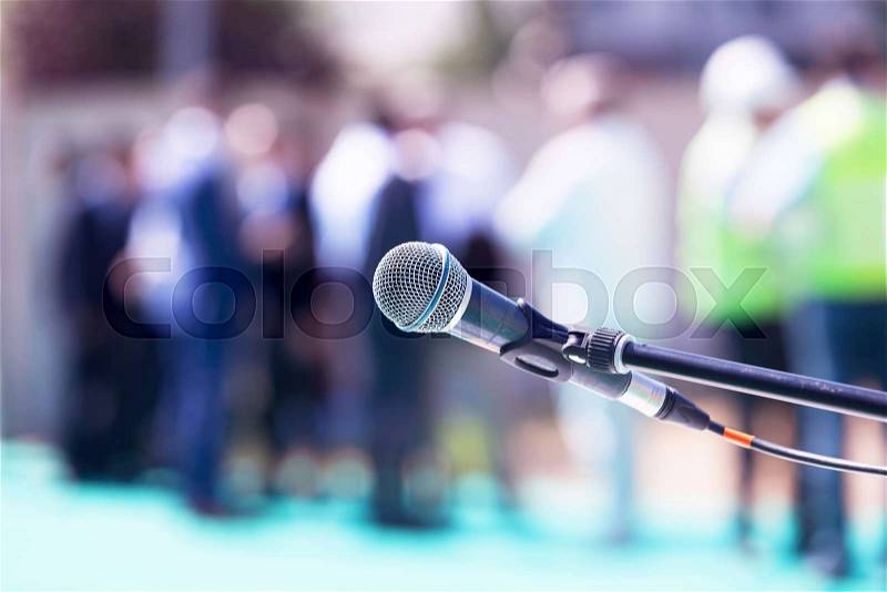 Microphone in focus against blurred group of people, stock photo