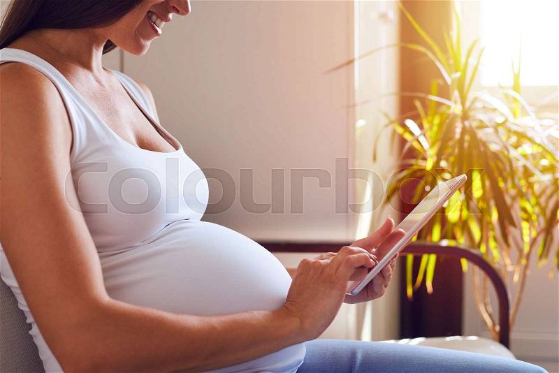 Cropped shot of mother-to-be using tablet with sunbeams on background , stock photo