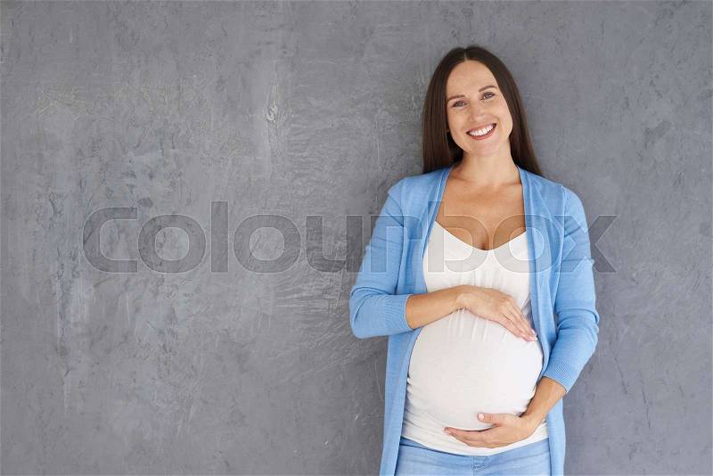 Portrait happy future woman posing with hands on belly at camera in studio, stock photo