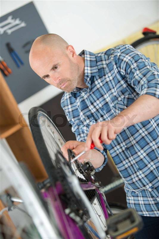 Handyman fixing bike wheel in his garage, stock photo