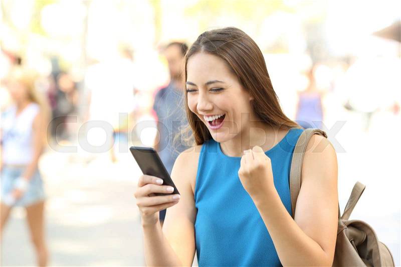 Excited woman reading amazing news on line in a smart phone on the street, stock photo
