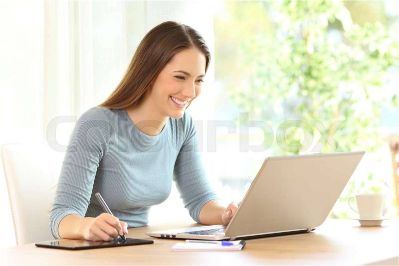 Happy woman drawing with a display pen and a laptop on a desk at home, stock photo