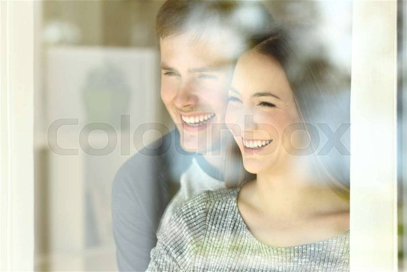 Portrait of a happy couple in love looking through a window at home or hotel interior, stock photo
