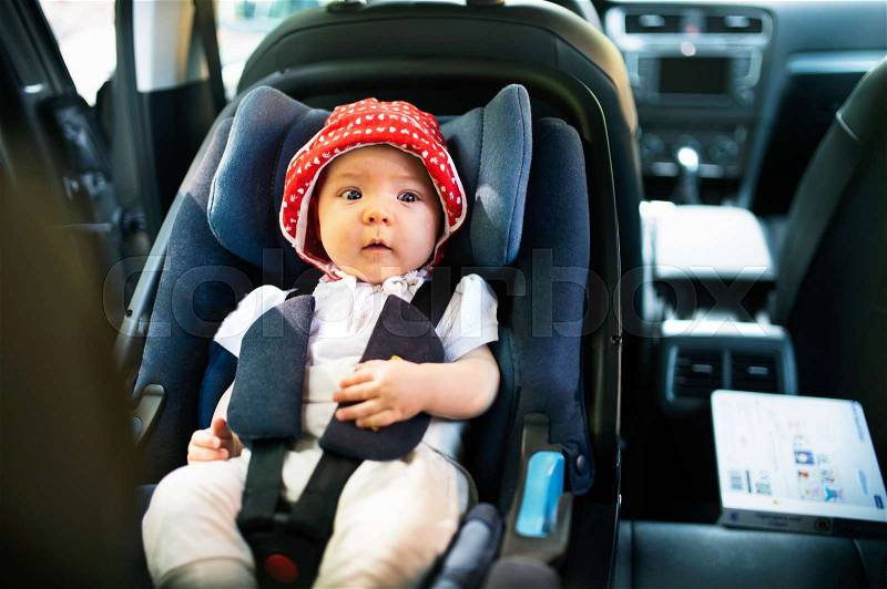 Cute little baby girl fastened with security belt in safety car seat, stock photo