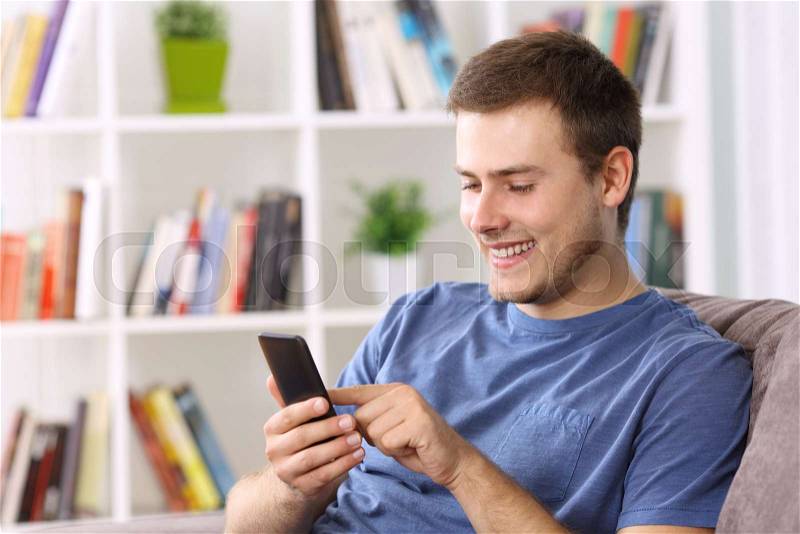 Happy guy using a smart phone on line sitting on a sofa at home, stock photo