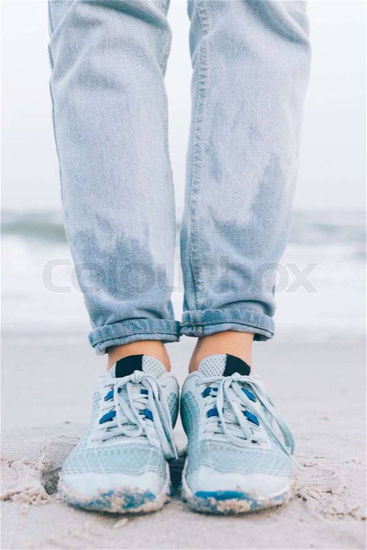 Female feet in wet sneakers and jeans on the beach, vertical framing, stock photo