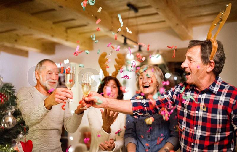 Senior friends with confetti and champagne next to Christmas tree, having fun, stock photo