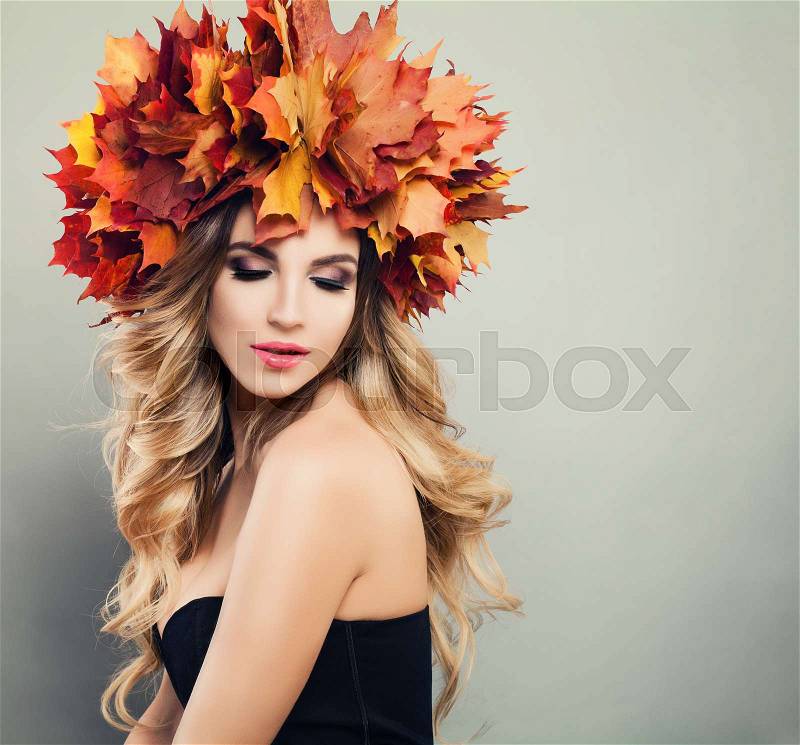 Autumn Beauty. Beautiful Woman Spa Model with Wavy Blonde Hair, Makeup and Fall Leaves Wreath on Gray Background with Copy space, stock photo