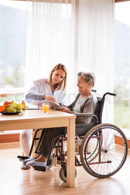 Health visitor and a senior woman with tablet during home visit. A nurse talking to an elderly woman, stock photo