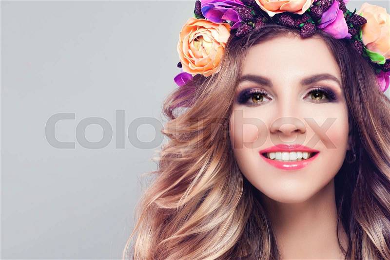 Young Beautiful Woman Smiling. Cute Model with Wavy Blonde Hair, Makeup and Colorful Flowers Wreath on Gray Background with Copy space, stock photo