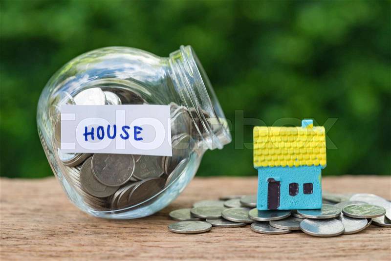 Glass jar bottle labeled as house with full of coins and miniature house on stack of coins as home, property or mortgage investment concept, stock photo