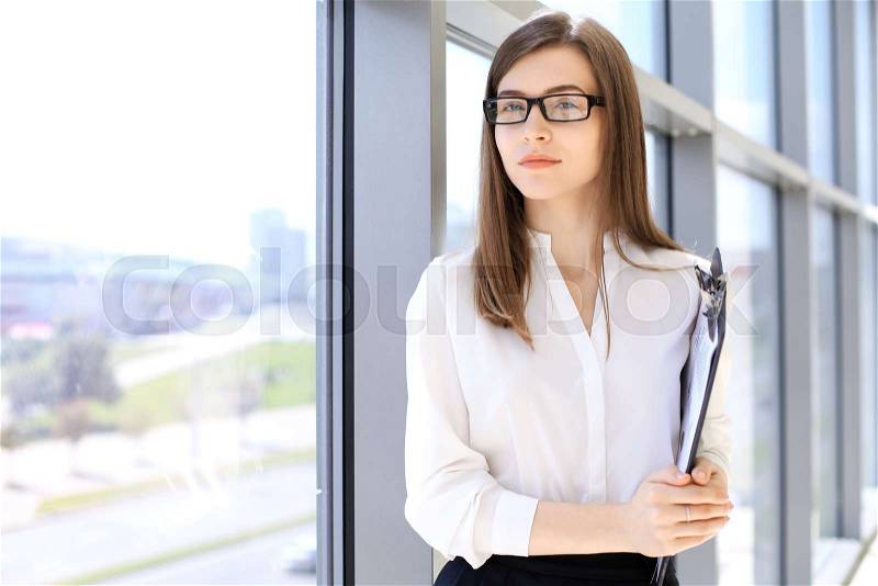 Modern business woman standing and keeping a clipboard in the office, stock photo