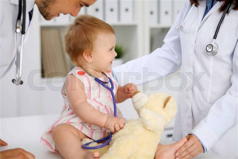 Happy cute baby at health exam at doctor\'s office. Toddler girl is sitting and keeping stethoscope and teddy bear, stock photo