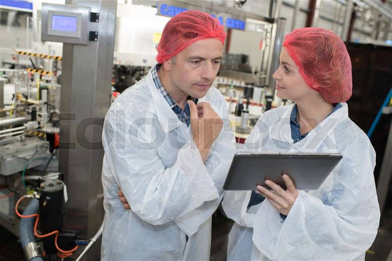 Male and female factory workers in discussion holding tablet, stock photo