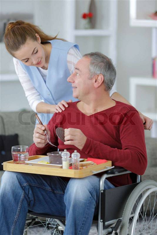 Young beautiful nurse helpping disabled elder man at home, stock photo