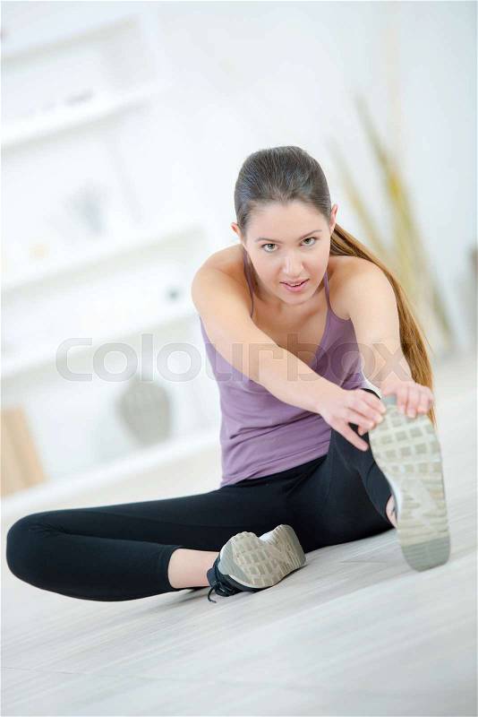 Young woman exercising at home stretching legs, stock photo