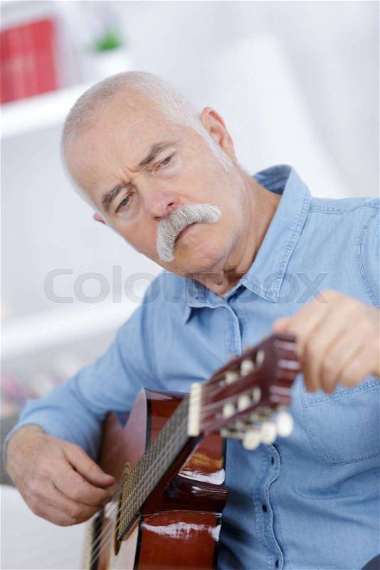 Senior man at home learning to play guitar, stock photo
