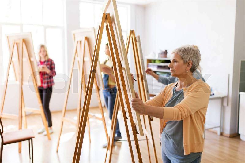 Art school, creativity and people concept - happy senior woman artist with easel and pencil drawing picture at studio, stock photo