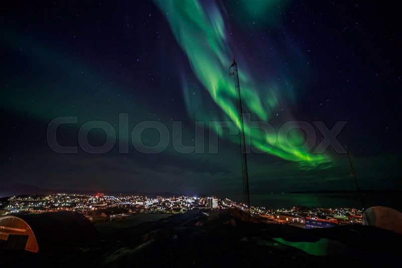 Green lights of Aurora Borealis with shining stars over the fjord and highlighted city, Nuuk, Greenland, stock photo