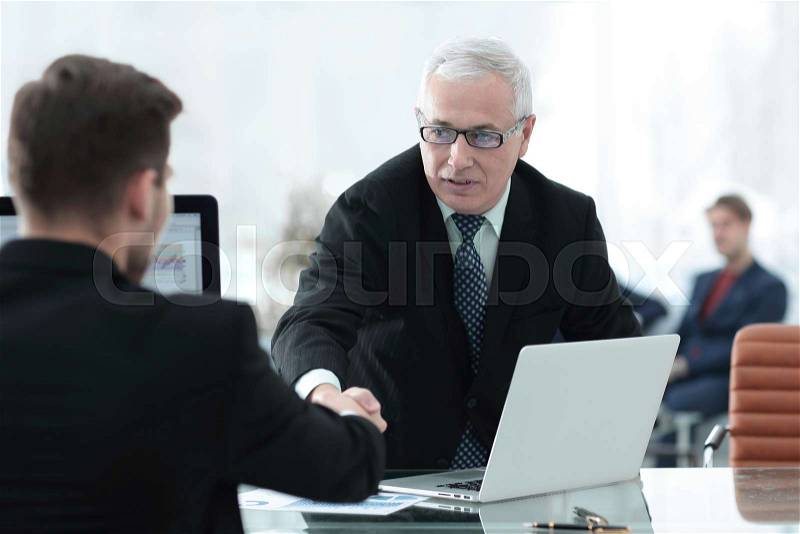 Businessman welcomes business partner shaking hands sitting behind a Desk in a modern office, stock photo