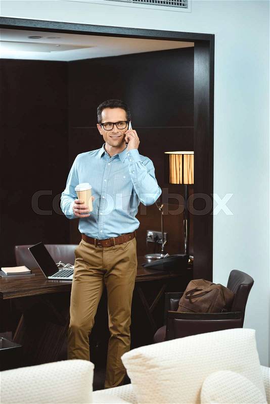 Businessman in business casual clothes talking on phone and holding cup of coffee, stock photo