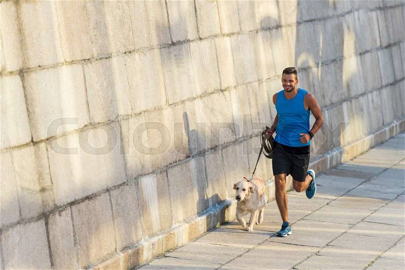 Athletic sportsman running with golden retriever dog at wall in city, stock photo