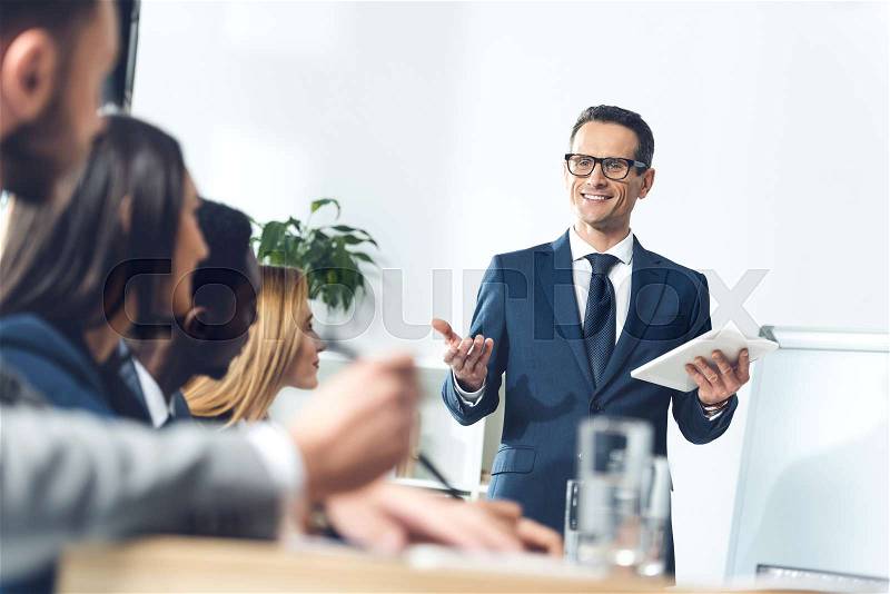 Happy handsome team leader with tablet talking to managers in conference hall, stock photo