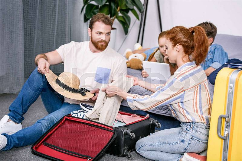 Happy family packing luggage for trip together in bedroom, stock photo