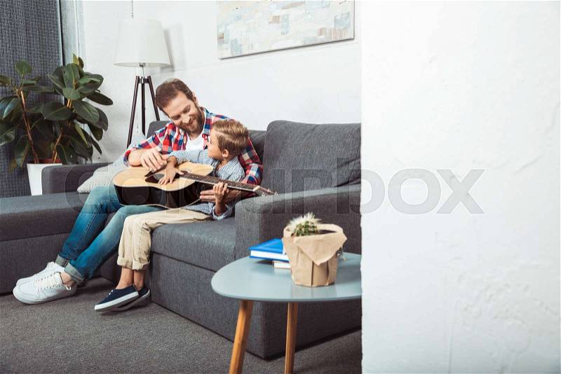 Happy father and son playing guitar and smiling each other at home, stock photo