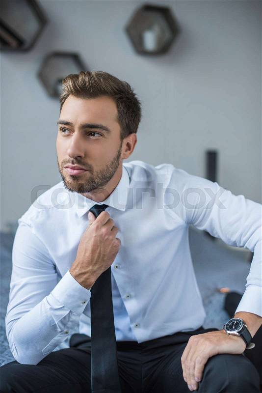 Young businessman in white shirt, straightening his tie and looking aside, stock photo