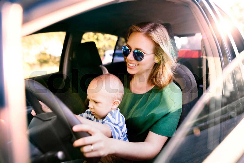 Young mother with her little son in the car. A woman and baby boy pretending to be driving, stock photo
