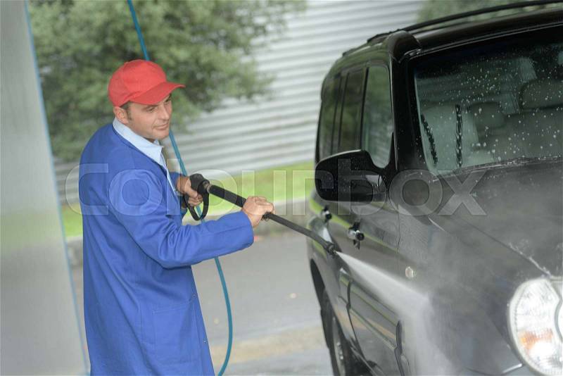 Man working with high pressure washer to clean a car, stock photo