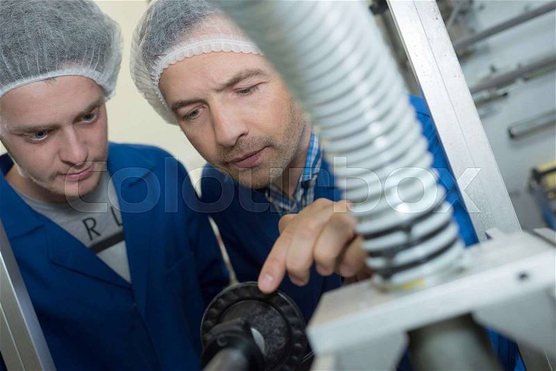 Two male wearing safety hair net working at a factory, stock photo