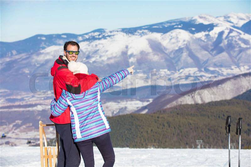 Rear view of a loving couple in fur hood jackets looking at snowed mountain range, stock photo