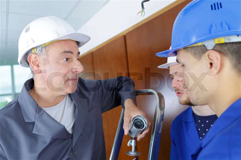 Technician telling students how to installing video surveillance camera, stock photo