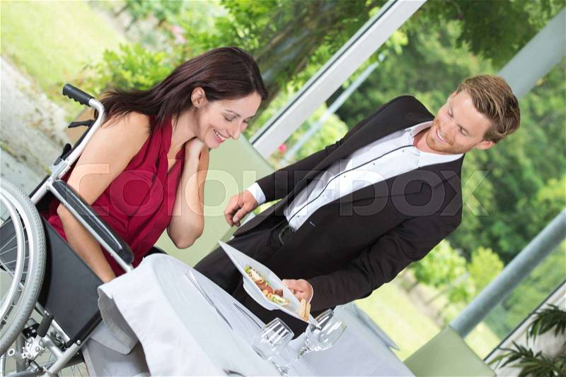 Handsome waiter bringing order to happy disabled mature female, stock photo