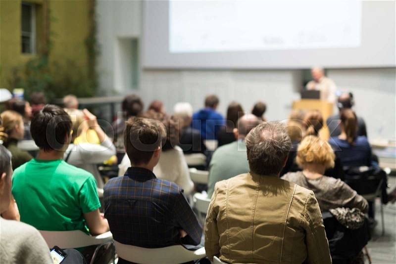 Male speaker giving presentation in lecture hall at university workshop. Audience in conference hall. Rear view of unrecognized participant in audience. Scientific conference event, stock photo