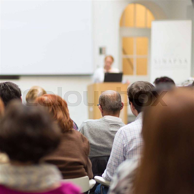 Female speaker giving presentation in lecture hall at university workshop. Audience in conference hall. Rear view of unrecognized participant in audience. Scientific conference event, stock photo
