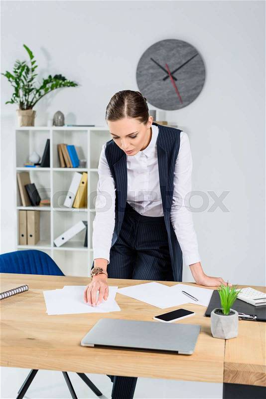 Young businesswoman in office standing over her desk, looking at paperwork, stock photo